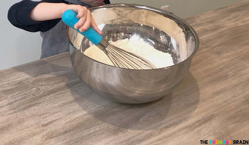 A childs hands mixing flour with a whisk